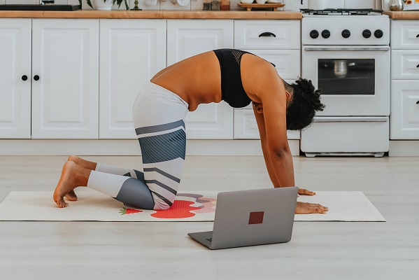 Vrouw op yogamat die oefeningen uitvoert met behulp van pc